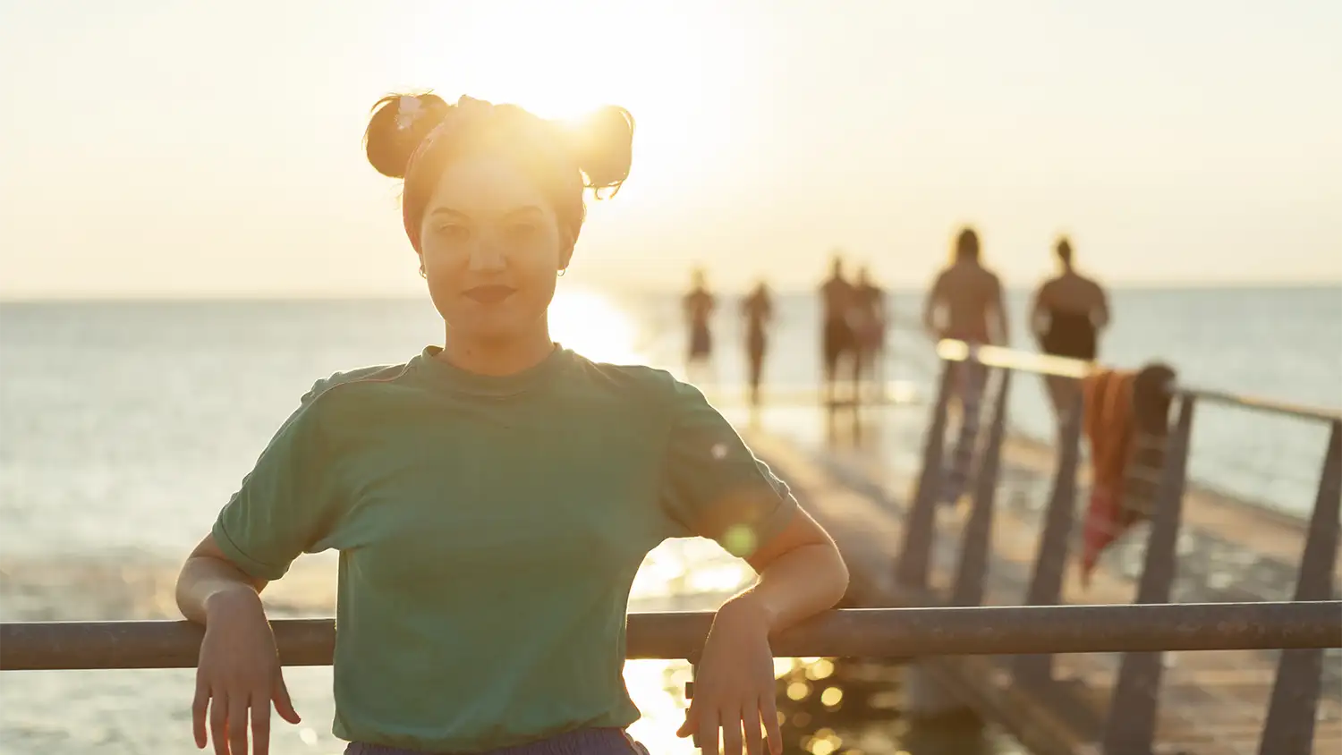 Una joven en un muelle durante el atardecer de verano, representando la importancia del autocuidado para la prevención de enfermedades como la meningitis.